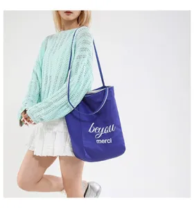 Detalle de un gran bolso de lona azul con el estampado 'merci' llevado por una modelo.