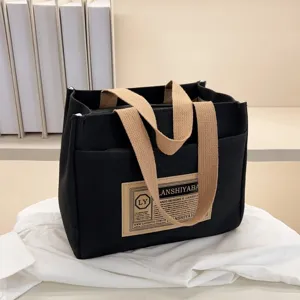 Close-up detail of a black canvas lunch bag featuring a vintage patch and beige woven straps