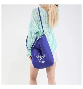 Vista de detalle de un gran bolso tote de lona azul con estampado Merci blanco en modelo