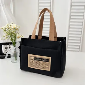 Detailed view of black canvas lunch tote with a vintage patch and brown straps