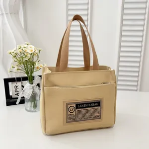 Close-up of beige canvas lunch bag with decorative black patch and sturdy handles.