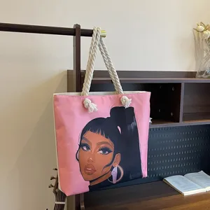 Detalle de un bolso tote rosa con estampado de chica negra y asas de cuerda.