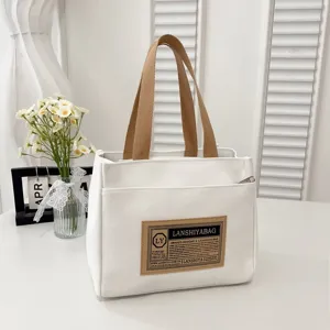 Detail view of the white canvas tote bag with brown handles and front patch decoration.
