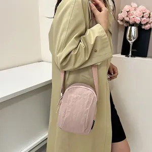 Primer plano de un bolso bandolera de nailon rosa impermeable combinado con una gabardina beige