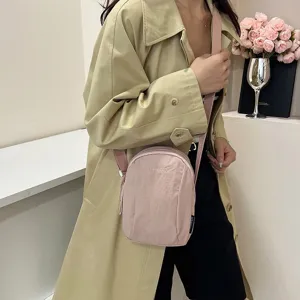 Primer plano de un bolso bandolera minimalista de nailon rosa con una gabardina verde claro