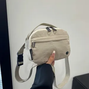 Vista detallada de un bolso bandolera beige de tela Oxford impermeable, sujeto a mano para escala