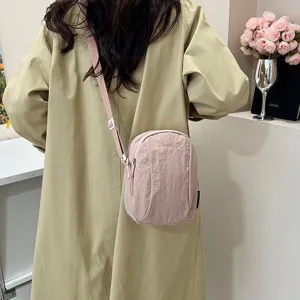 Vista trasera de un bolso bandolera de nailon rosa impermeable en una modelo con gabardina