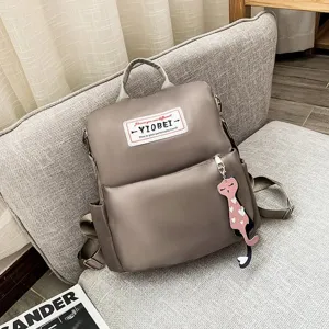 Taupe waterdichte Oxford rugzak voor dames met roze kattenhanger op een bank
