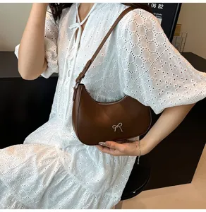 Detailweergave van een bruine hobo-tas met strik gedragen bij een witte kanten jurk