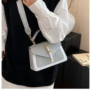 Detalle del bolso bandolera cuadrado pequeño gris con textura tejida y una correa ancha