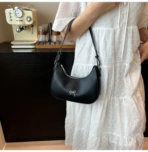 Elegante zwarte onderarmtas met een zilveren strik gedragen door een mooi model