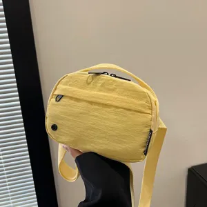 Vista detallada de un bolso bandolera de tela oxford amarilla impermeable sujeta con la mano.