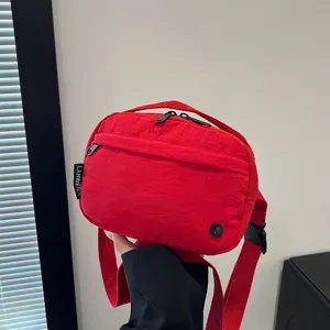 Detalle de un bolso bandolera rojo de tela oxford impermeable con cremalleras negras
