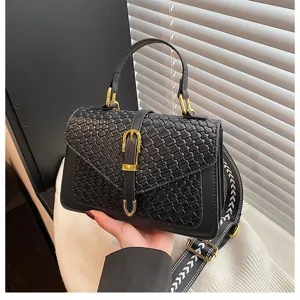 Detalle de bolso trenzado negro con hebilla dorada y correa de hombro ancha estampada.