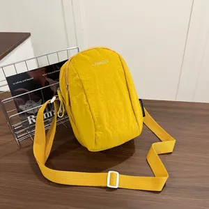 Foto lifestyle de un bolso bandolera de nailon amarillo sobre escritorio de madera.
