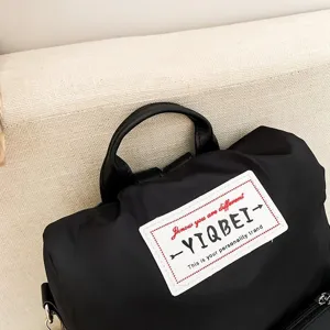 Detailopname van de decoratieve logopatch en oxford-stof op een zwarte casual rugzaktas