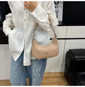 Minimalistische beige hobo-onderarmtas met een delicaat zilveren strikje gedragen door model