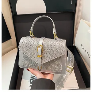 Detalle de un bolso bandolera gris con patrón trenzado y hebilla dorada elegante