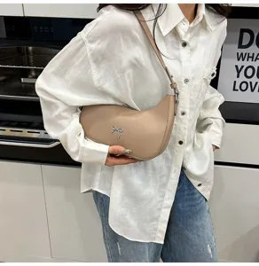 Detail van een chique beige hobo-tas met zilveren strik, gedragen als schoudertas
