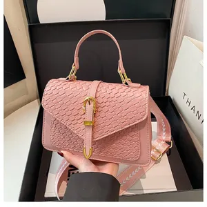 Vista detallada del bolso de mano rosa con textura tejida, hebilla dorada y correa ancha de moda
