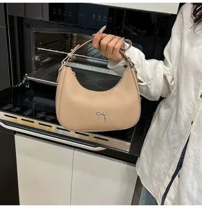 Detailopname van een beige hobo-tas met een stijlvolle zilveren strik-bedeltje