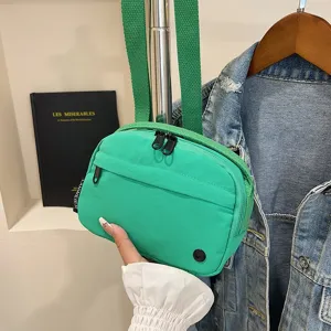 Vista detallada de un bolso bandolera de tela oxford verde impermeable sostenido con la mano