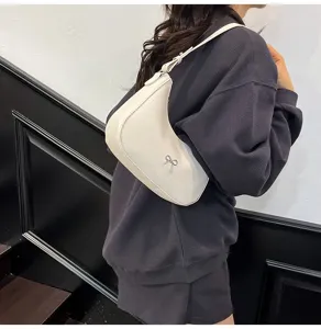 Detailopname van een witte zadeltas onder de arm met een zilveren strikje.