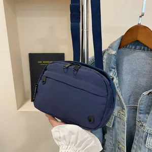 Vista detallada de un bolso bandolera azul marino de tela Oxford impermeable sostenido a mano.