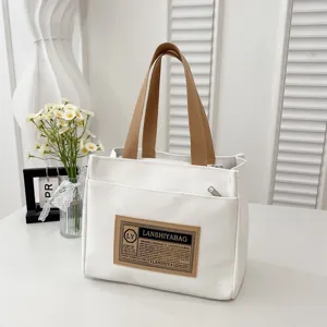 Detailed view of a white canvas tote bag with brown handles and a vintage front patch.