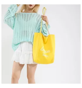 Bolso tote de lona amarillo con estampado be you merci llevado por una modelo en atuendo casual