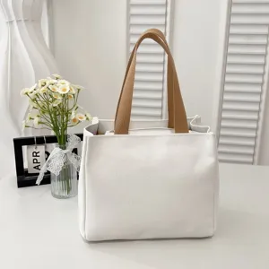 A minimalist white canvas lunch bag with brown handles displayed in a cozy home setting