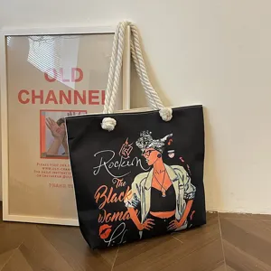 Bolso tote negro con estampado gráfico y asas de cuerda apoyado en una pared