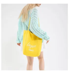 Vista lateral de una modelo con un bolso tote de lona amarillo vibrante con texto blanco.