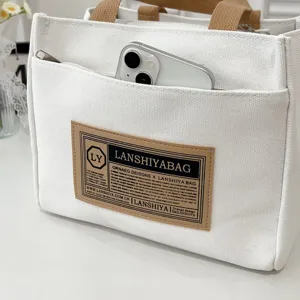 Close-up detail of white canvas tote bag with front zipper pocket and stylish label