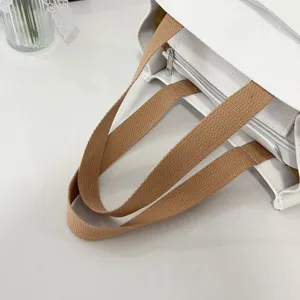 Detailed view of durable brown woven handles and internal zipper on white canvas bag