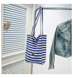 Detalle de un bolso tote de lona a rayas azules y blancas colgado en un perchero.