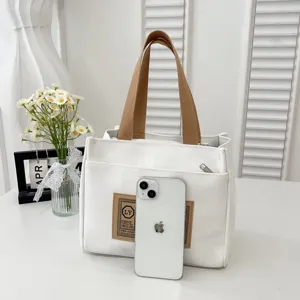 Detailed view of white canvas tote bag with brown handles and iPhone for size reference