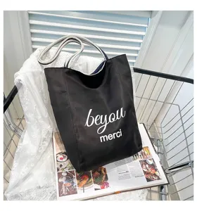Bolso tote de lona negra con frase 'beyou merci' y asas de cuerda a rayas.