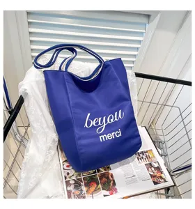 Detalle de bolso tote de lona azul grande con estampado merci blanco y asas de cuerda