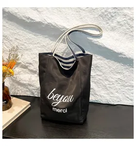 Bolso tote de lona negra con texto 'beyou merci' e interior a rayas