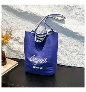 Vista detallada del bolso tote de lona azul con estampado 'merci' y asas de rayas