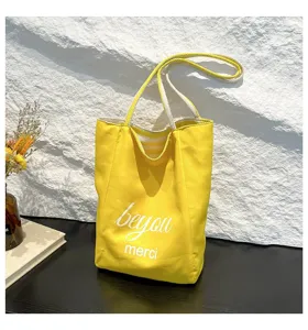 Bolso tote de lona amarillo vibrante con asas a rayas y detalle impreso "beyou merci"