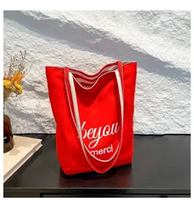 Bolso tote de lona rojo vibrante con asas a rayas y estampado blanco en un escritorio negro.