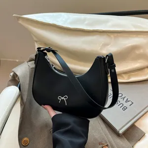 Elegante zwarte zadeltas met zilveren strikdetail in een lifestyle-omgeving