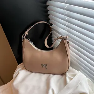 Detailweergave van een stijlvolle beige zadeltas met een zilveren strikdecoratie.