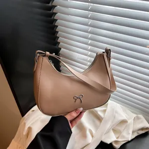 Detailopname van een bruine hobo tas met een zilveren strik ornament in de hand.