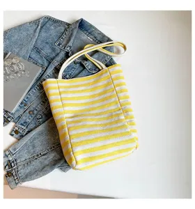 Bolso tote de lona a rayas amarillas y blancas con asas de cuerda sobre fondo vaquero.