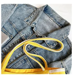 Detalle del asa del bolso tote de lona a rayas amarillas sobre una chaqueta vaquera