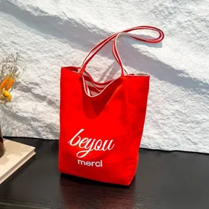 Bolso tote de lona roja con asas a rayas y elegante estampado blanco 'beyou merci'.
