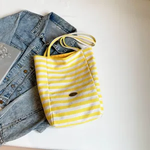 Bolso tote de lona a rayas amarillas y blancas con asas de cuerda y chaqueta vaquera azul